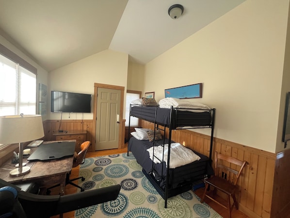 A room with bunk beds, a desk with a chair, a television, and a door.