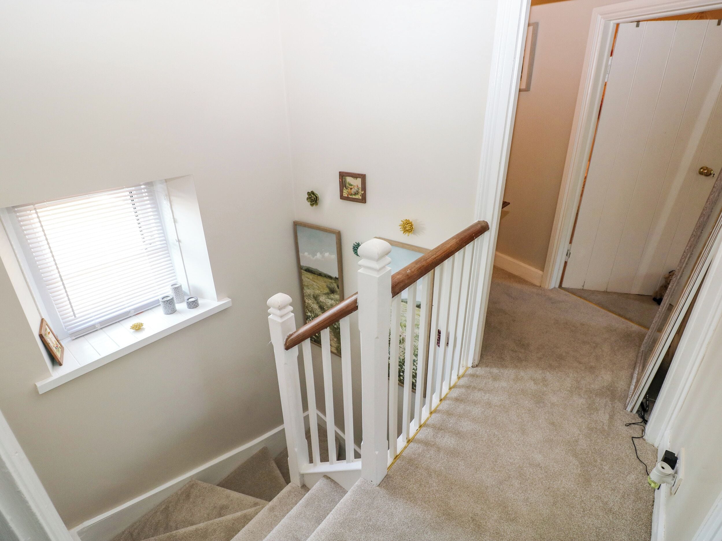 A staircase with a white railing, carpeted steps, a window with blinds, and a door in the background.