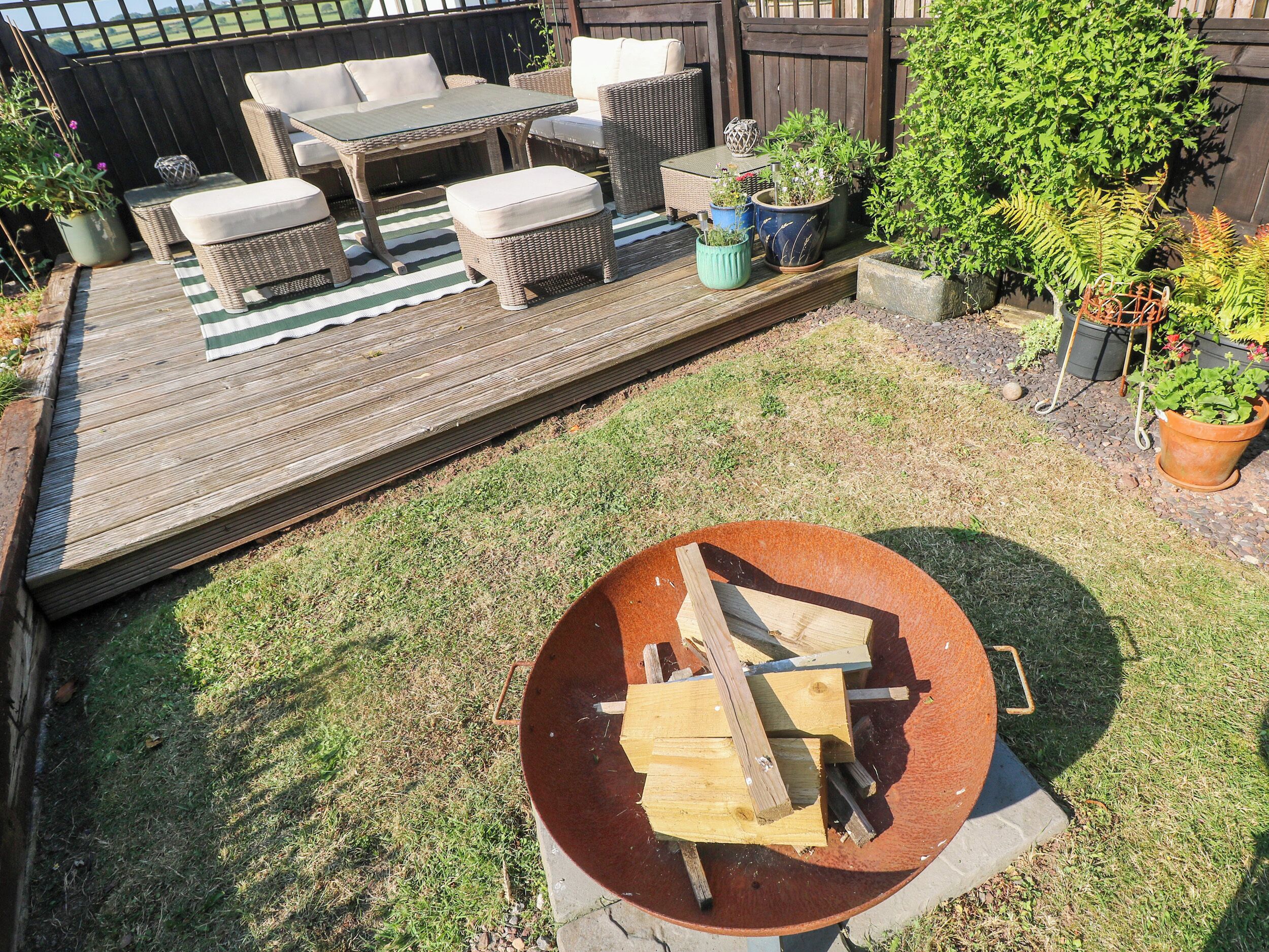 Een houten terras met tuinmeubilair, een vuurkorf en potplanten.