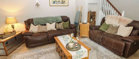 Uma sala de estar com dois sofás de couro marrom, uma mesa de centro de madeira, um tapete estampado, um abajur e um quadro na parede.