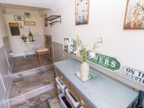 A hallway with a wooden chair, a white vase with flowers, and a green sign on the wall. - St.twynells Farm (Pembroke)