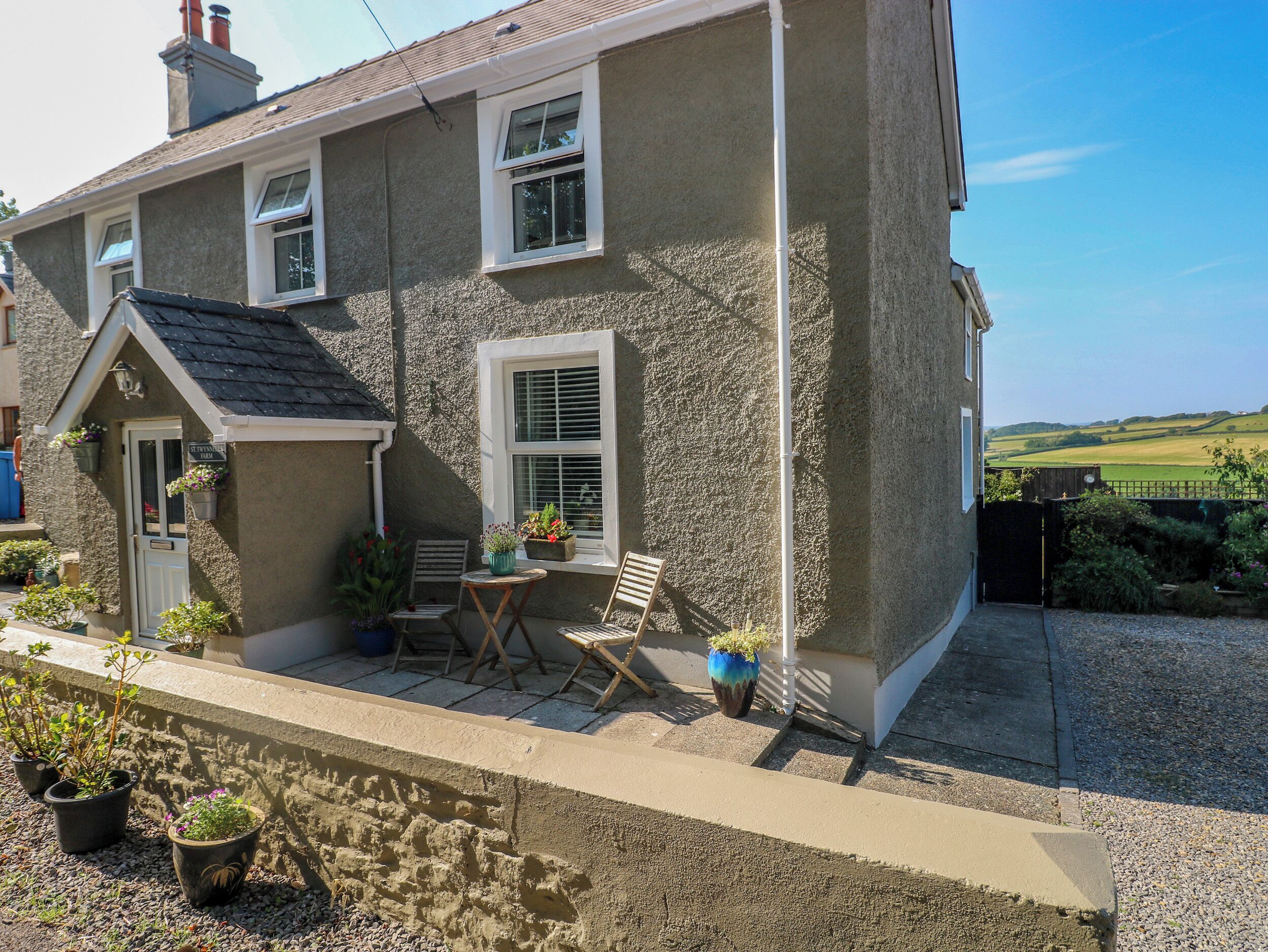 Une maison à deux étages avec un petit patio, une porte avec une enseigne et une vue sur la campagne.
