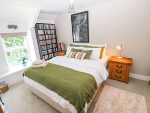 Ein Schlafzimmer mit Bett, Nachttisch, Lampe, Bücherregal und Fenster.