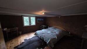 Ein Schlafzimmer mit einem Bett, einem Fenster, einem Gemälde, einem Holzboden und einem Kuhfellteppich.