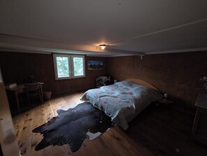 Makuuhuoneessa on sänky, ikkuna, taulu, puulattia ja lehmännahkamatto.
