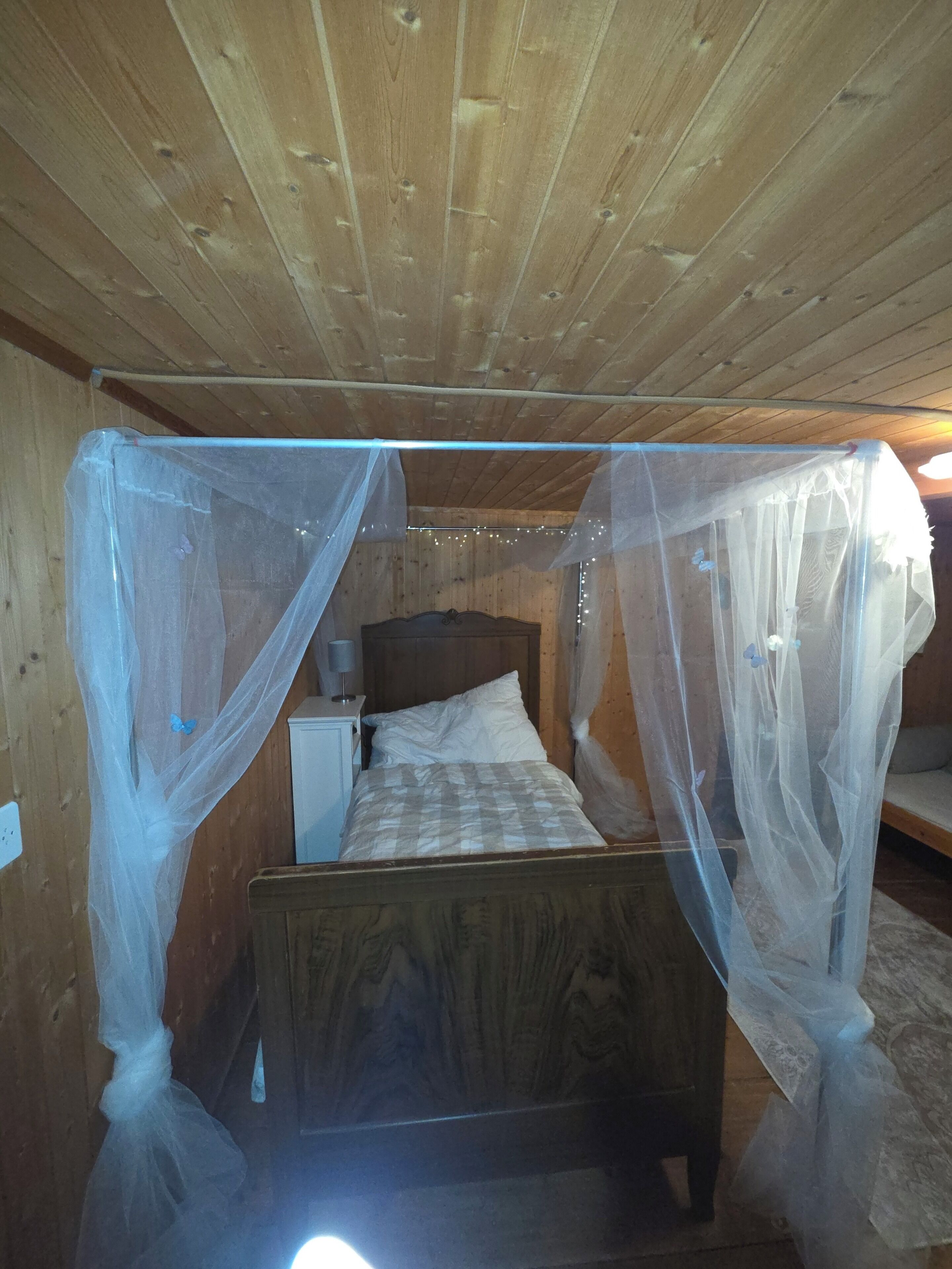 Ein Zimmer mit Holzboden, einem Bett unter einem Moskitonetz, einem Nachttisch und einer Lampe.