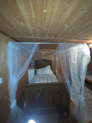 Une pièce en bois avec un lit recouvert d’une moustiquaire, une table de chevet et une lampe.