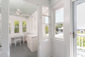 Ein Zimmer mit weißem Schreibtisch, Stuhl und Einbauschränken. Mehrere Fenster sorgen für natürliches Licht und Ausblicke.