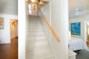 Eine Treppe mit weißen Stufen und einem orangefarbenen Geländer, die zu einem Schlafzimmer mit einem Bett und einem Bild an der Wand führt.