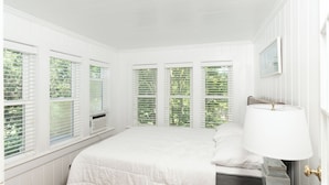 Une chambre à coucher avec un lit, une table de chevet, une lampe et des fenêtres équipées de stores.