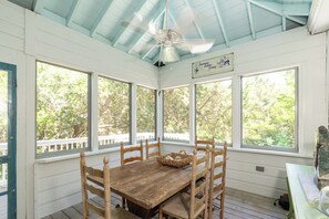 Eine überdachte Veranda mit einem Holztisch und Stühlen, großen Fenstern und einem Deckenventilator.