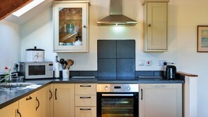 A kitchen with a microwave, toaster, and oven. There is a cabinet with glassware and a black countertop. - Stunning Bamburgh Coast Apartment (Okehampton)