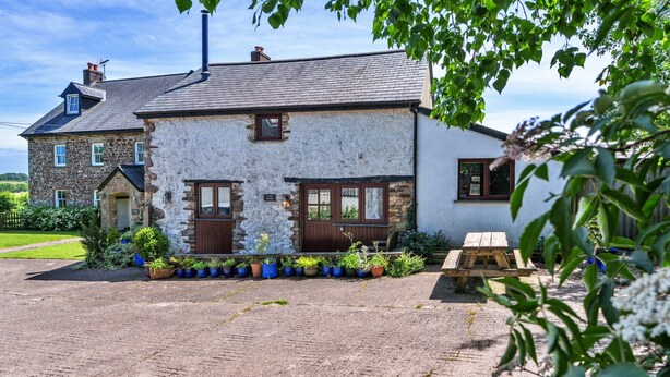 A two-story stone building with a slate roof, a wooden door, and a small window. - Stunning Bamburgh Coast Apartment (Okehampton)