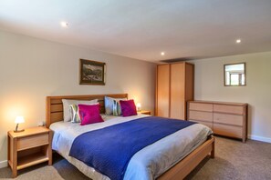 A bedroom with a bed, nightstands, a wardrobe, and a painting on the wall. - Stunning Bamburgh Coast Apartment (Okehampton)