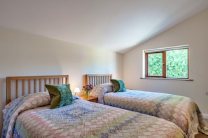 Ein Zimmer mit zwei Betten, jeweils mit einem Holz-Kopfteil, einem Nachttisch mit Lampe und einem Fenster mit Blick auf Grünflächen.