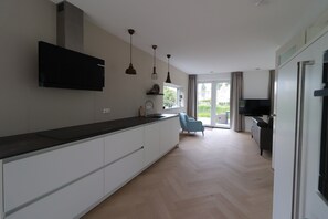 A modern kitchen with a flat-screen TV, pendant lights, and a view to the outside. - Private Bungalow With Jetty for 6 (Makkum)