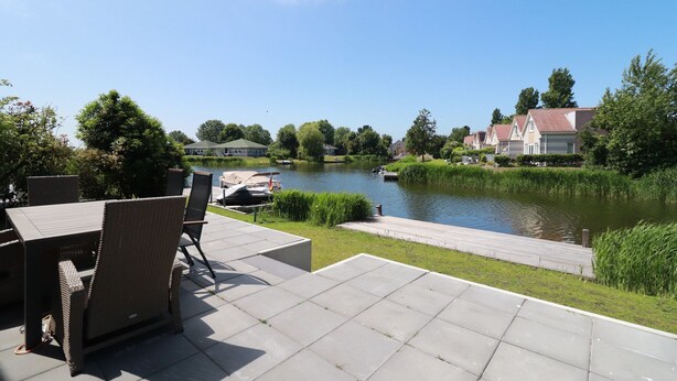 A riverside patio with outdoor furniture, a wooden dock, and houses in the background. - Private Bungalow With Jetty for 6 (Makkum)