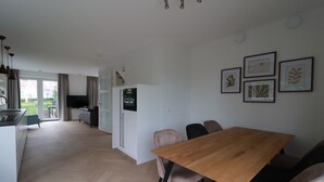 A modern kitchen with a built-in oven, a dining area with a wooden table and chairs, and a view of the outdoors through large windows. - Private Bungalow With Jetty for 6 (Makkum)