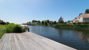 A wooden dock extending into a calm river, surrounded by greenery and residential buildings. - Private Bungalow With Jetty for 6 (Makkum)