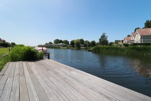 Eine Holzstege reicht in einen ruhigen Fluss, umgeben von Grünflächen und Wohnhäusern.