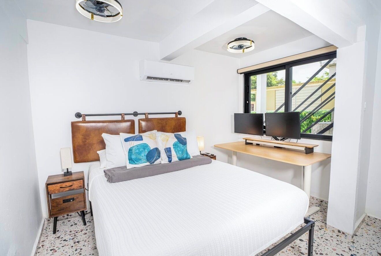 A bedroom with a bed, bedside table, lamp, TV, and a window with a view.