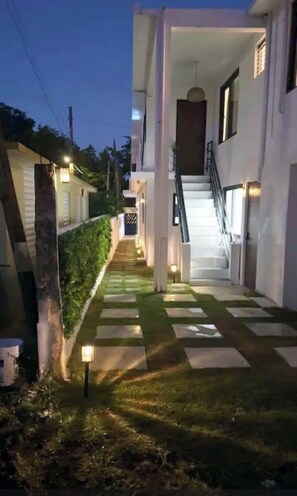 Ein Weg führt zu einer Treppe vor einem modernen Gebäude mit weißer Fassade und einem verschlossenen Eingang.