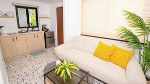 A compact living space with a kitchenette, a sofa with yellow cushions, a coffee table, and a potted plant. - Beachfront Bliss: 2BR Family-Friendly Retreat unit 1 (Dorado)
