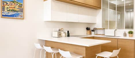 A modern kitchen with white cabinetry, a central island with bar stools, and a large window.