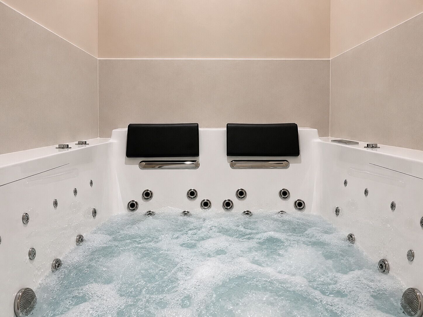 A modern bathroom with a large bathtub, two black control panels, and multiple water jets.