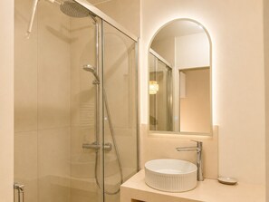Ein modernes Badezimmer mit einer gläsernen Duschkabine, einem runden Waschbecken und einem Spiegel mit integrierter Beleuchtung.