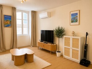 A modern living room with a flat-screen TV, a potted plant, and a vacuum cleaner. - Bail mobilité - Bel appart 1 ch Panier avec clim (Marseille)