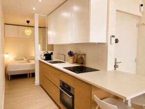 A modern kitchen with a built-in oven, a sink, and a dining area with a chair. - Bail mobilité - Bel appart 1 ch Panier avec clim (Marseille)