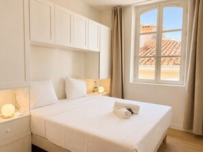 A hotel room with a bed, bedside table, lamp, and a window with curtains. - Grand T4 vue Major • Panier • Clim • 6 pers (Marseille)