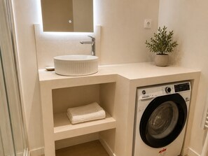 A compact bathroom with a sink, mirror, potted plant, and a washing machine. - Grand T4 vue Major • Panier • Clim • 6 pers (Marseille)