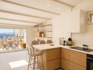 A modern kitchen with wooden cabinets, a central island, and a view of the sea. - Grand T4 vue Major • Panier • Clim • 6 pers (Marseille)
