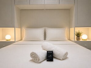 A neatly made bed with white linens and pillows, a rolled towel, a welcome box, and bedside lamps with spherical light fixtures. - Grand T4 vue Major • Panier • Clim • 6 pers (Marseille)