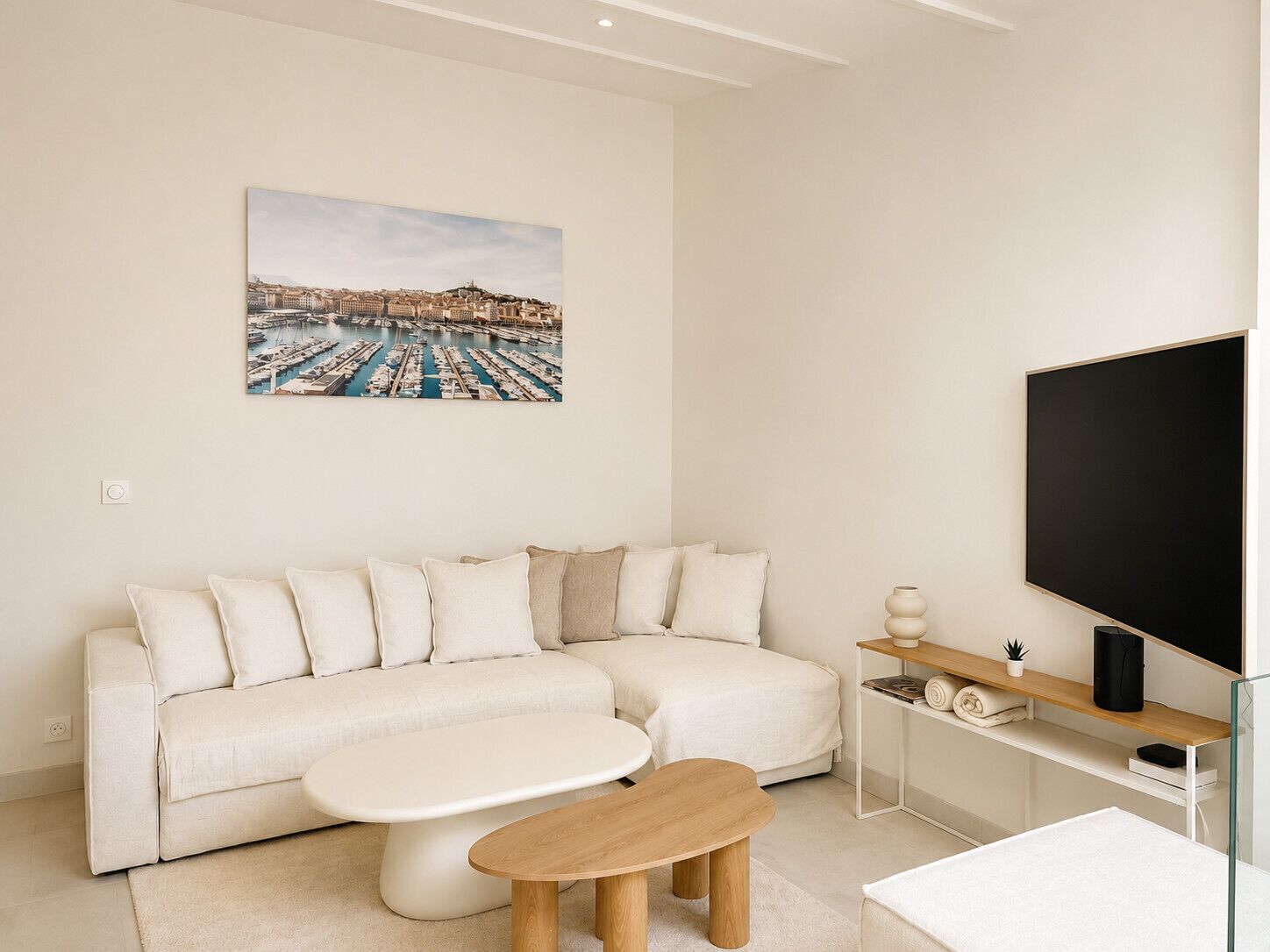 Un salon moderne comprenant un canapé, une table basse, un téléviseur à écran plat et un tableau représentant un port de plaisance.