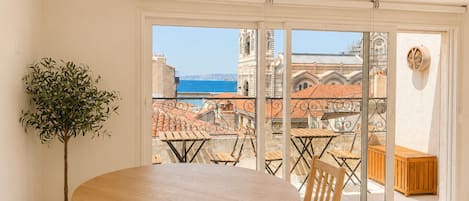 A balcony with a table and chairs, a potted plant, and a view of a historic building and the sea.