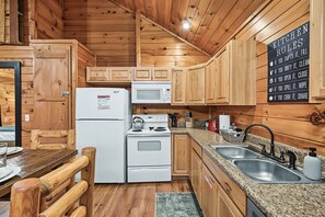 A compact kitchen with wooden cabinets, a refrigerator, microwave, stove, and a sink. - Cozy Couples Cabin | Fireplace + Hot Tub (Sevierville)