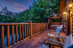 A wooden deck with a railing, a seating area with chairs, and a building with a window. - Romantic Fall Cabin | Hot Tub + Fireplace (Sevierville)