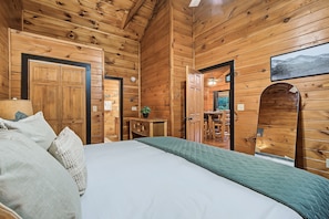 A wooden cabin room with a bed, a small table, and a chair. - Cozy Couples Cabin | Fireplace + Hot Tub (Sevierville)