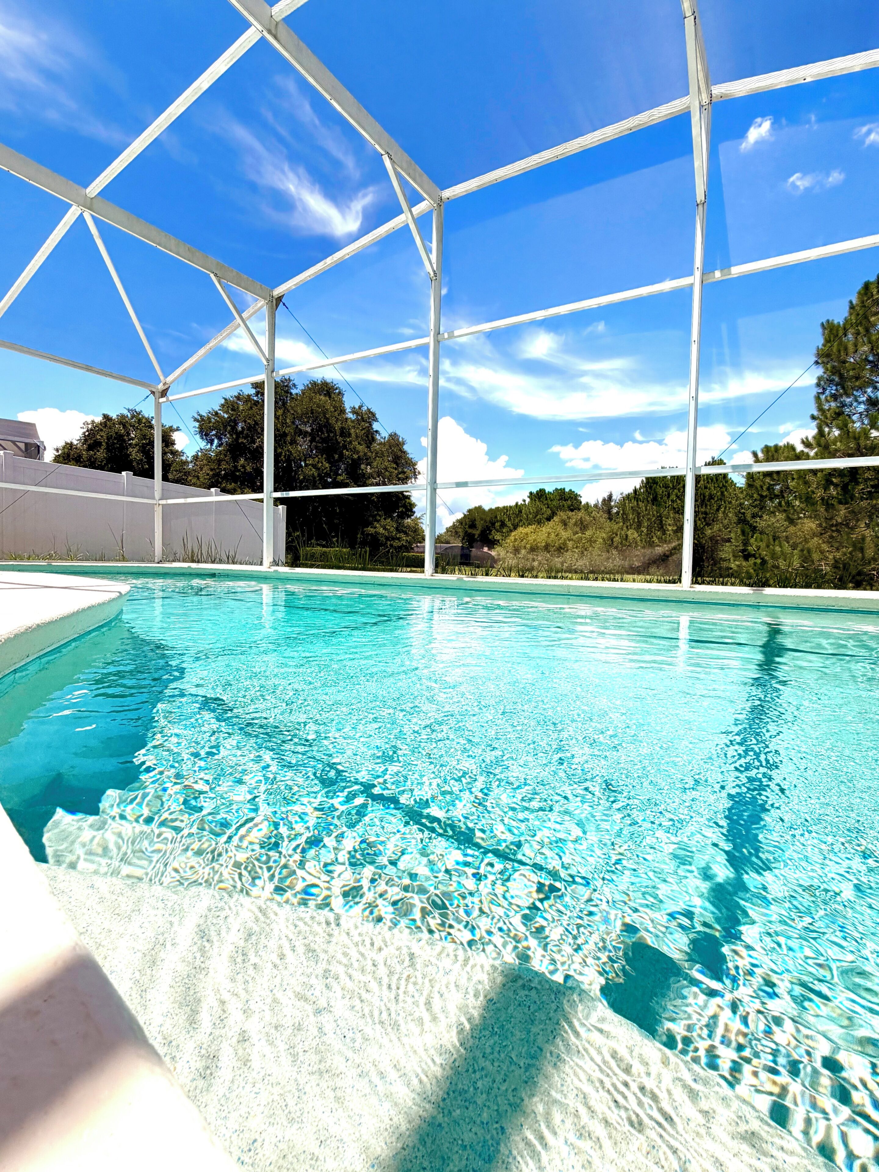 A swimming pool with a clear blue water surface, surrounded by a white structure, and trees in the background.