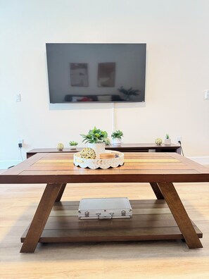 A wooden dining table with a tray of decorative items, a flat-screen TV mounted on the wall, and a small potted plant on the table. - 4BR Family Retreat/ Private Pool/ Kids' Chill Room/ Preserve View (Clermont)