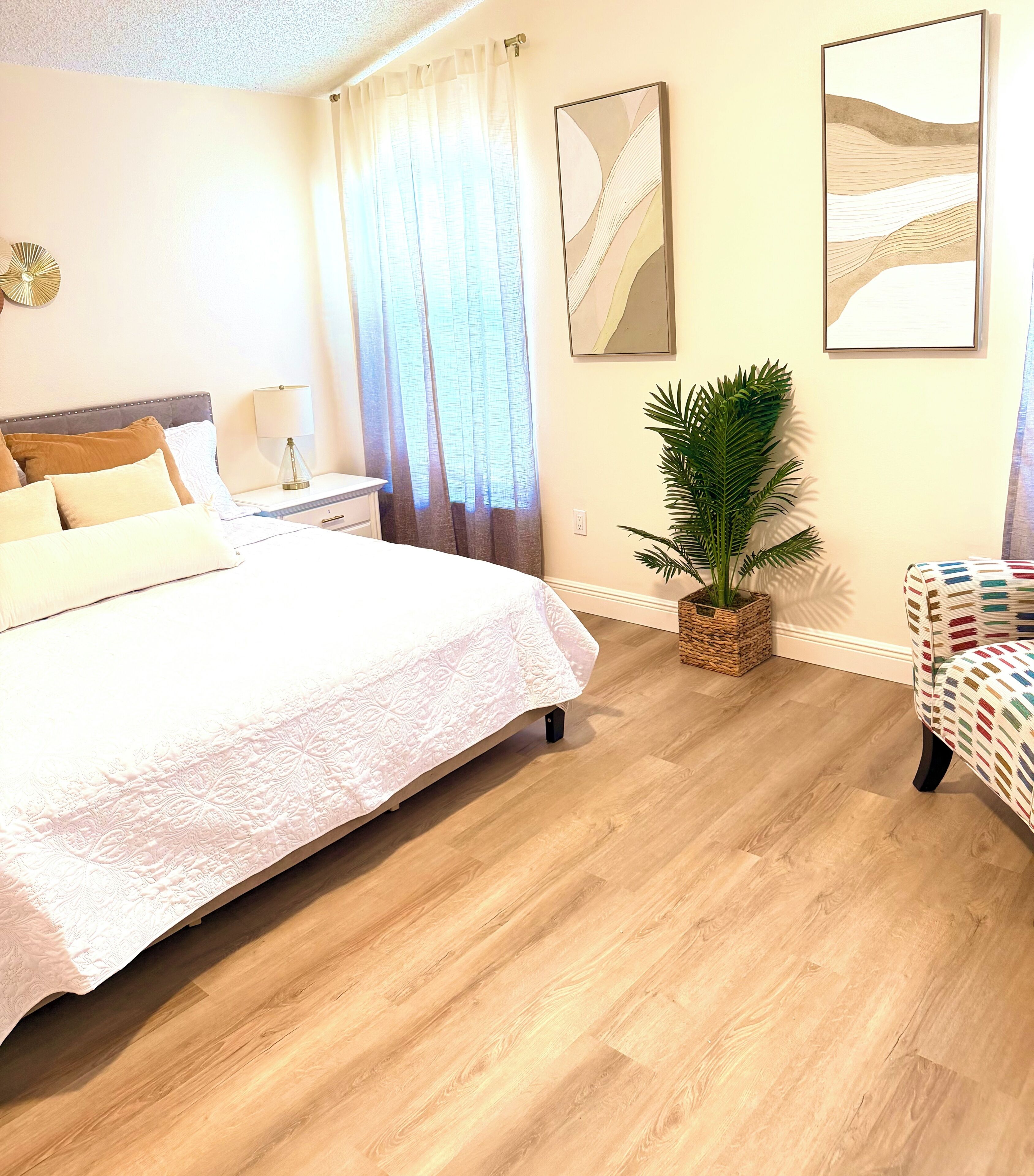 A hotel room with a bed, a nightstand, a lamp, a potted plant, and a chair.