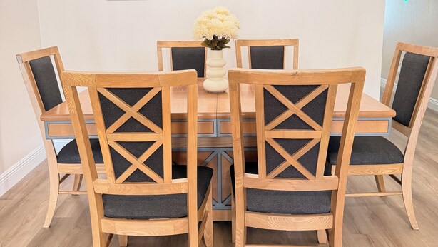 Uma sala de jantar com uma mesa redonda, seis cadeiras de madeira com encosto em forma de cruz e um vaso de flores.
