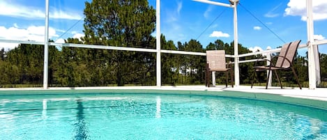 A clear blue pool with a white structure overhead, surrounded by trees and a clear sky.