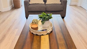 Uma sala de estar com um sofá marrom, duas almofadas, uma planta em vaso, uma bandeja com um controle remoto e uma bola decorativa.