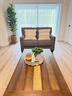 Ein Wohnzimmer mit einem braunen Sofa, zwei Kissen, einer Topfpflanze, einem Tablett mit einer Fernbedienung und einer dekorativen Kugel.