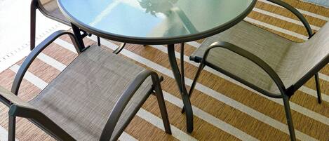 A round glass table with four chairs, a potted plant, and a view of a pool.