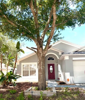 A residential house with a large tree in front, a red door, and a garage. - 4BR Family Retreat/ Private Pool/ Kids' Chill Room/ Preserve View (Clermont)